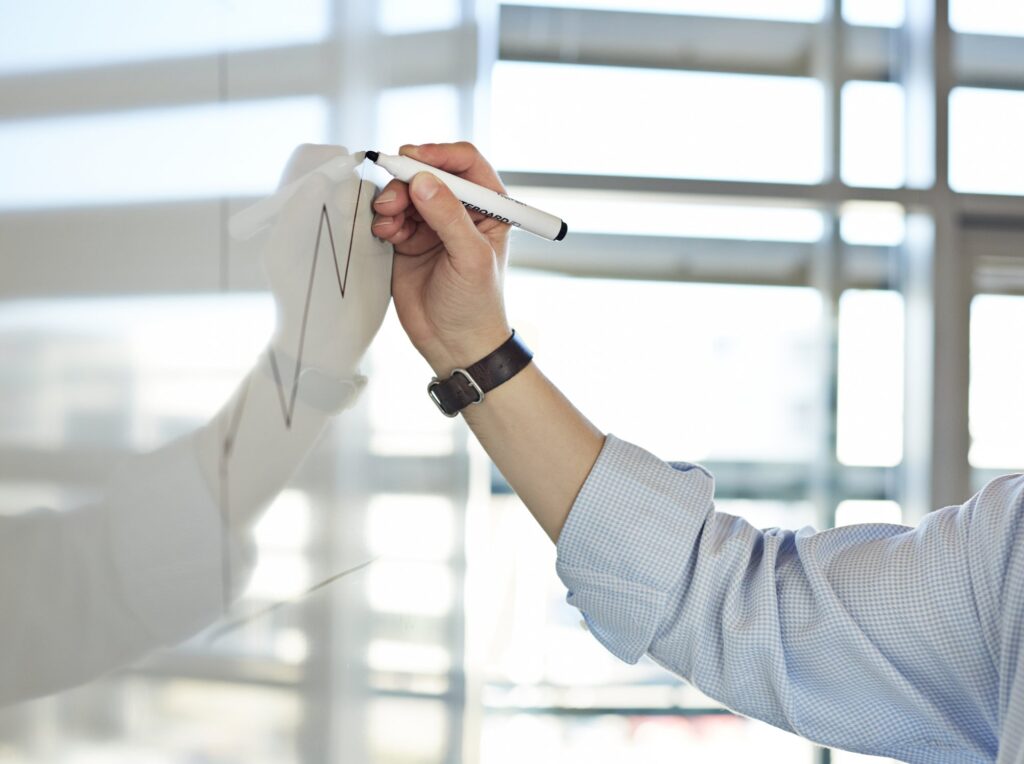 Hand draws graph on whiteboard in an office environment.