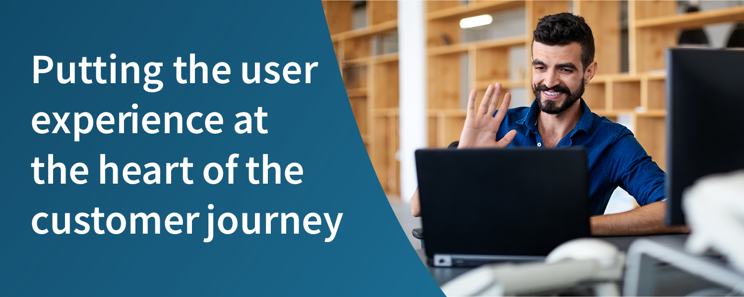 Enhancing the customer experience strategy: prioritising the user experience. Man wearing a blue shirt in an office, waving to a colleague on his laptop screen.